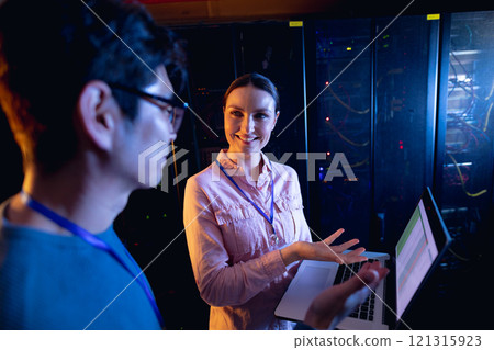 Diverse male and female engineers using laptop in computer server room 121315923