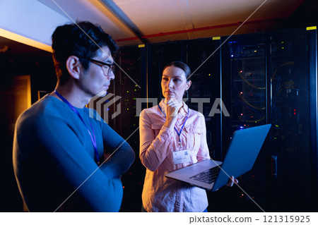 Diverse male and female engineers using laptop in computer server room 121315925