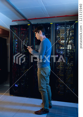 Asian male engineer writing on clipboard in computer server room 121315940