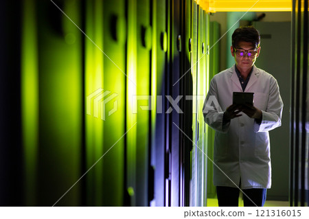 Asian male engineer wearing an apron using digital tablet while inspecting in computer server room 121316015