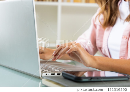 Woman typing on laptop at home, smartphone nearby on desk 121316290
