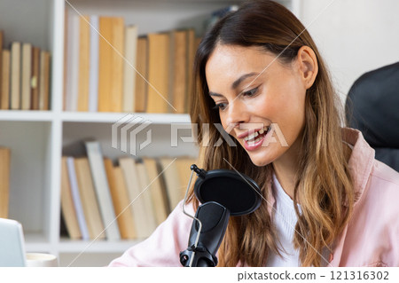 Woman recording podcast at home, smiling and speaking into microphone 121316302
