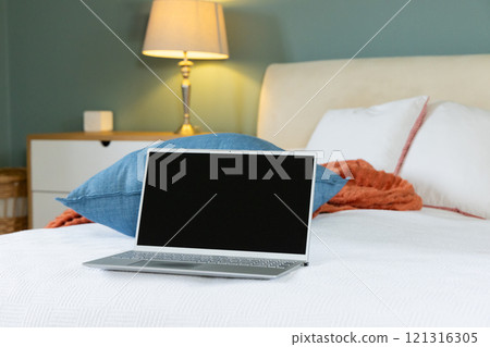 Laptop resting on cozy bed in warmly lit bedroom, ready for work, at home, copy space 121316305