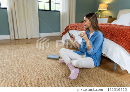 Relaxing at home, woman enjoying coffee and browsing smartphone by bed Relaxing at home, woman enjoying coffee and browsing smartphone by bed 121316313