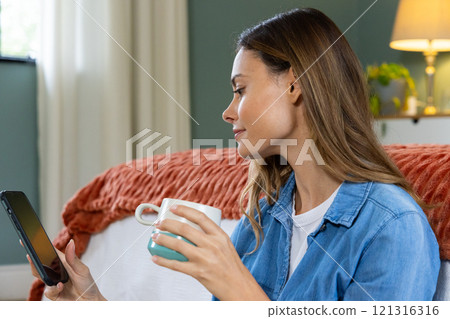 Relaxing at home, woman enjoying coffee while browsing tablet in cozy room Relaxing at home, woman enjoying coffee while browsing tablet in cozy room 121316316