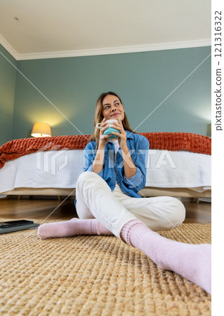 Relaxing at home, woman enjoying hot drink sitting on bedroom floor 121316322
