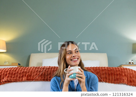 Smiling woman enjoying coffee in cozy bedroom, feeling relaxed and content, at home 121316324