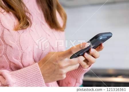 Woman in pink sweater texting on smartphone at home during Christmas season Woman in pink sweater texting on smartphone at home during Christmas season 121316361