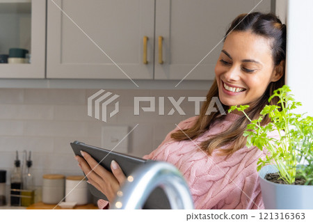 Smiling woman in kitchen reading tablet near potted plant, enjoying leisure time, at home Smiling woman in kitchen reading tablet near potted plant, enjoying leisure time, at home 121316363