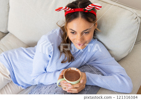 Christmas time, Relaxing on sofa, woman wearing festive headband enjoying hot chocolate at home Christmas time, Relaxing on sofa, woman wearing festive headband enjoying hot chocolate at home 121316384