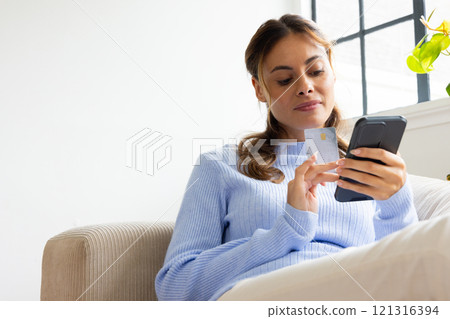 At home, woman using smartphone and credit card for online shopping, copy space 121316394