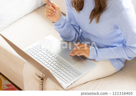 Woman in blue sweater using laptop on couch, working from home 121316405