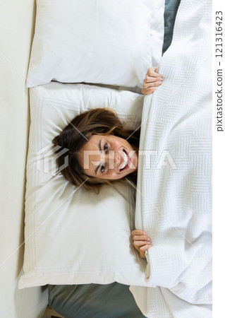 Smiling woman in bed enjoying cozy morning under white blanket at home 121316423