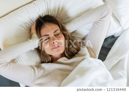 Woman lying in bed covering ears, feeling stressed and frustrated at home 121316440