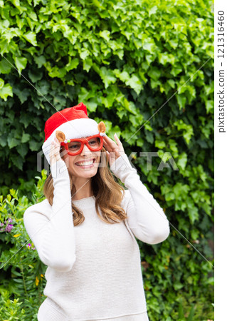 Christmas time, Wearing Santa hat and festive glasses, woman smiling outdoors in holiday spirit 121316460