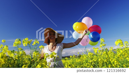 Woman walking with colorful balloons in mustard field on a sunny day Woman walking with colorful balloons in mustard field on a sunny day 121316692