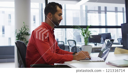 Biracial businessman sitting at desk using laptop Biracial businessman sitting at desk using laptop 121316714