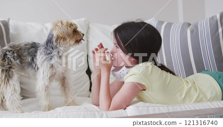 Caucasian girl spending time at home, lying on sofa with face mask, playing with pet dog, in slow mo Caucasian girl spending time at home, lying on sofa with face mask, playing with pet dog, in slow mo 121316740