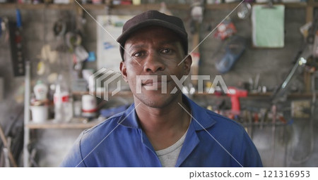 Portrait of a happy African male panel beater in a township workshop, wearing a cap, looking at came Portrait of a happy African male panel beater in a township workshop, wearing a cap, looking at came 121316953