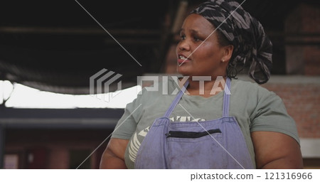 Front view of an African female butcher wearing a headscarf in a township workshop, cutting fresh me Front view of an African female butcher wearing a headscarf in a township workshop, cutting fresh me 121316966