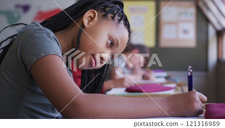 Biracial girl writing in a book while sitting on her desk at school Biracial girl writing in a book while sitting on her desk at school 121316989