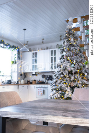 Grey Wooden empty table to demonstrate product with space for text with upholstered chairs in white kitchen, modern interior with Christmas tree and fairy lights. New Year, Christmas mood, cozy home. Grey Wooden empty table to demonstrate product with space for text with upholstered chairs in white kitchen, modern interior with Christmas tree and fairy lights. New Year, Christmas mood, cozy home. 121318365