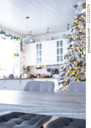 Grey Wooden empty table to demonstrate product with space for text with upholstered chairs in white kitchen, modern interior with Christmas tree and fairy lights. New Year, Christmas mood, cozy home. Grey Wooden empty table to demonstrate product with space for text with upholstered chairs in white kitchen, modern interior with Christmas tree and fairy lights. New Year, Christmas mood, cozy home. 121318374