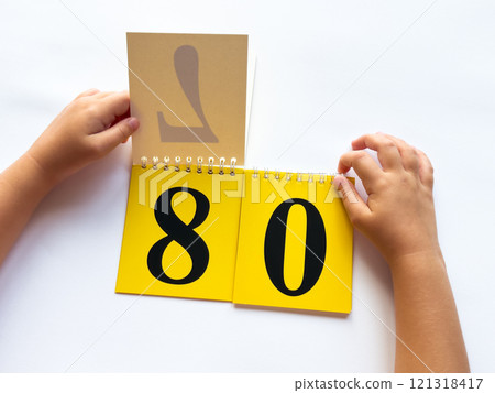 Childs hands flip through yellow pages with numbers. Displaying number 80 on white background 121318417