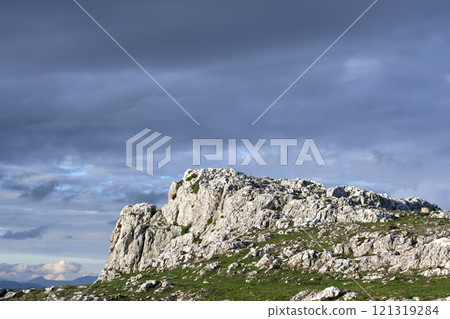 Rocky landscape with grassy foreground and dramatic cloudy sky 121319284