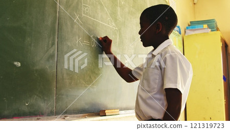 Side view close up of a young African schoolboy standing at the front of the class writing an answer Side view close up of a young African schoolboy standing at the front of the class writing an answer 121319723