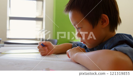 Side view of cute Asian schoolboy studying at desk in classroom at school Side view of cute Asian schoolboy studying at desk in classroom at school 121319855