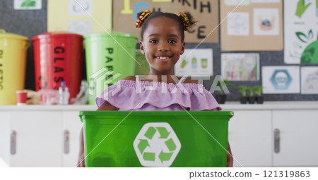 Happy african american schoolgirl standing in classroom, smiling, holding recycling bin Happy african american schoolgirl standing in classroom, smiling, holding recycling bin 121319863
