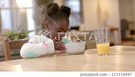 African american girl eating cereal with milk in kitchen 121319897