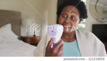 African american senior woman measuring her temperature while sitting on the bed at home African american senior woman measuring her temperature while sitting on the bed at home 121319959