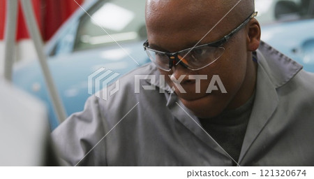 African American male car mechanic working in a township workshop, holding a screwdriver, using a ha African American male car mechanic working in a township workshop, holding a screwdriver, using a ha 121320674