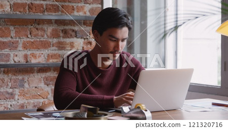 Front view of biracial man with short dark hair, working at home, sitting at the table in his sittin Front view of biracial man with short dark hair, working at home, sitting at the table in his sittin 121320716