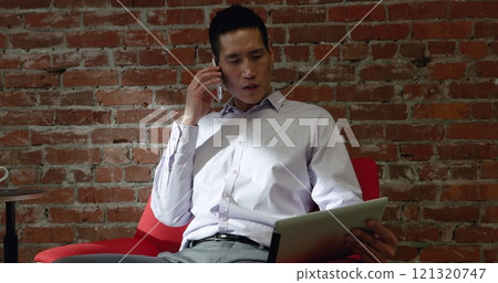 Front view close up of a biracial male business professional sitting in an armchair in a modern offi 121320747
