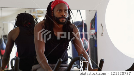 Male boxer exercising on exercise bike in fitness studio Male boxer exercising on exercise bike in fitness studio 121320787