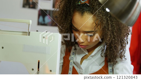 Front view of African American female fashion designer working with sewing machine in workshop Front view of African American female fashion designer working with sewing machine in workshop 121320843
