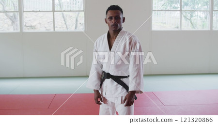 Front view of a teenage Biracial male judoka wearing white judogi, warming up before a training in a 121320866
