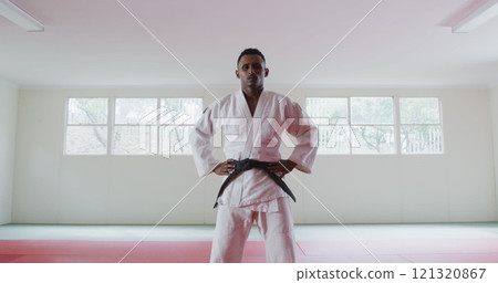 Portrait of a confident teenage biracial male judoka wearing white judogi, standing in the gym with 121320867