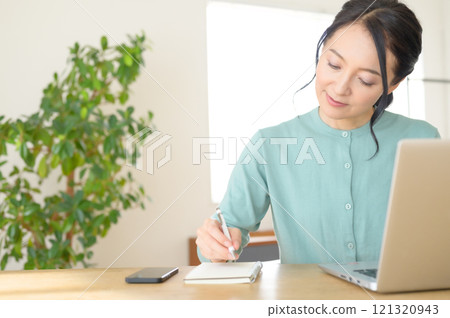 A middle-aged woman taking notes while looking at a computer 121320943