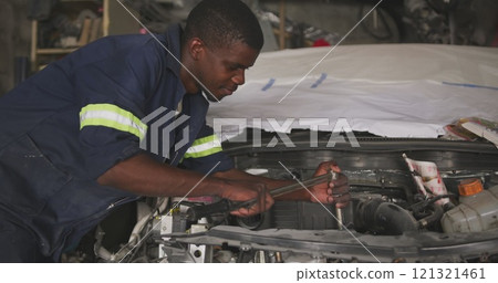 Side view of an African male car mechanic in a township workshop, repairing a car with a car boot op 121321461