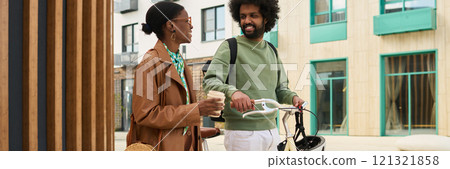 Two friends walking together while carrying coffee and a bicycle, having an engaging conversation in front of a modern building with wood and glass decor Two friends walking together while carrying coffee and a bicycle, having an engaging conversation in front of a modern building with wood and glass decor 121321858