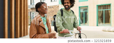 Two friends enjoying an outdoor walk, one holding a bicycle and other carrying a drink. Both are interacting and smiling while engaging in friendly banter Two friends enjoying an outdoor walk, one holding a bicycle and other carrying a drink. Both are interacting and smiling while engaging in friendly banter 121321859