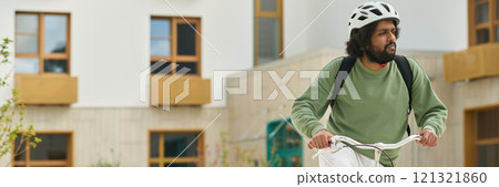 Man wearing helmet and backpack riding bicycle in urban environment with modern buildings in background looking focused and determined Man wearing helmet and backpack riding bicycle in urban environment with modern buildings in background looking focused and determined 121321860
