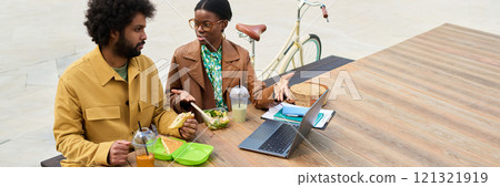 Two coworkers sitting at picnic table during lunch break outside, engaging in conversation about work projects while enjoying sandwiches and drinks Two coworkers sitting at picnic table during lunch break outside, engaging in conversation about work projects while enjoying sandwiches and drinks 121321919