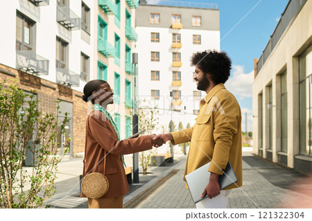 Two professionals exchanging handshake outdoors near modern apartment structures, initiating collaborative conversation in urban environment 121322304