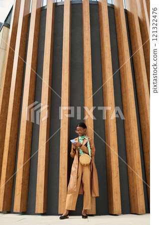 Person engrossed in reading magazine while standing against modern architectural structure. Minimalist background with wooden vertical lines Person engrossed in reading magazine while standing against modern architectural structure. Minimalist background with wooden vertical lines 121322476