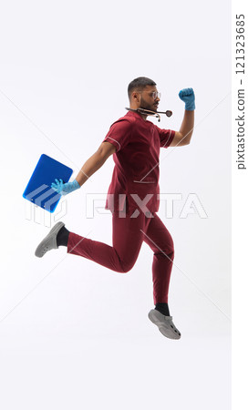 Young Indian man, dressed as doctor in uniform running, hurry up to patient against white studio background. Hospital. Young Indian man, dressed as doctor in uniform running, hurry up to patient against white studio background. Hospital. 121323685